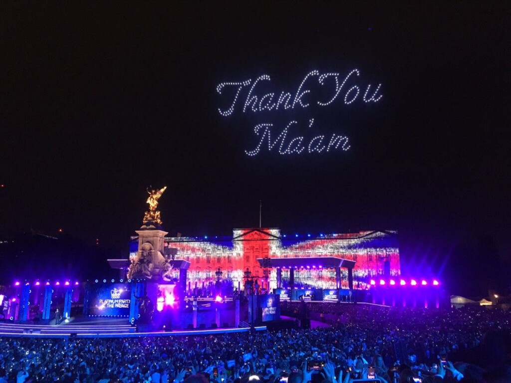 ユニオンジャックにライトアップされたバッキンガム宮殿と、その上の夜空に”Thank you Ma’am ”の文字を描くドローンの光