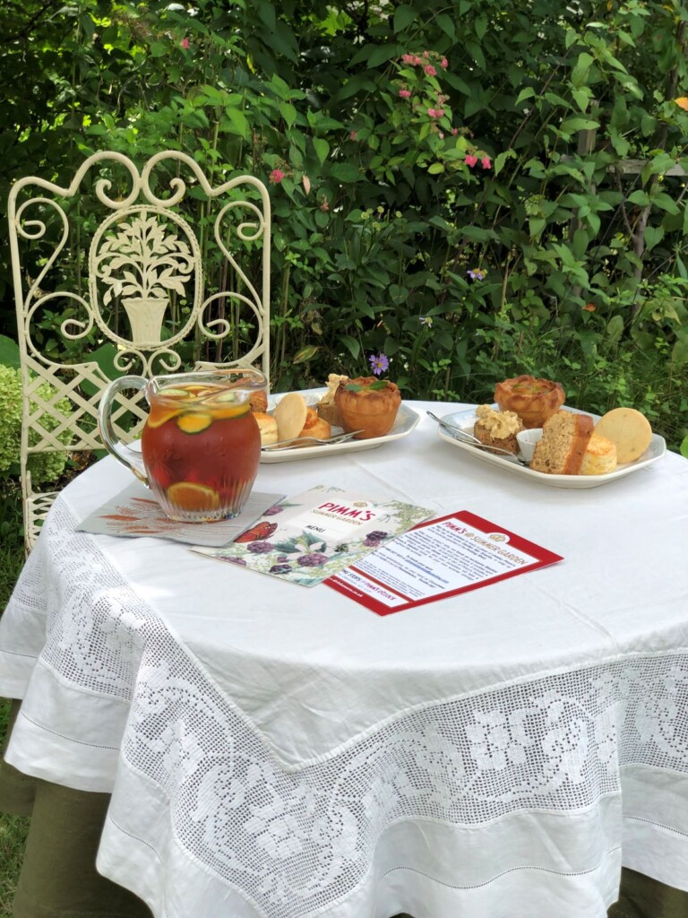 ガーデンに置かれた白いクロスがかかったテーブルに置かれたピムズティーとセイボリーや英国菓子のワンプレート