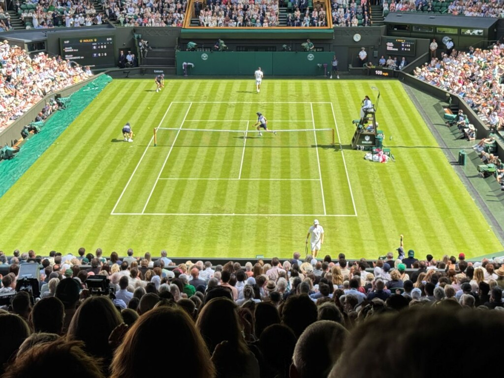 緑の芝が鮮やかなウィンブルドンのセンターコートと白のウェアでプレイするテニス選手